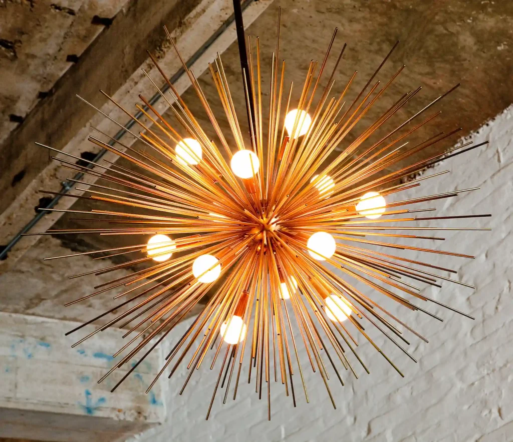 Starburst chandelier with glowing bulbs and radiating metal rods hanging from the ceiling.