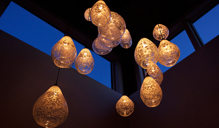 Cluster of glowing glass pendant lights suspended near tall windows against a dark ceiling.
