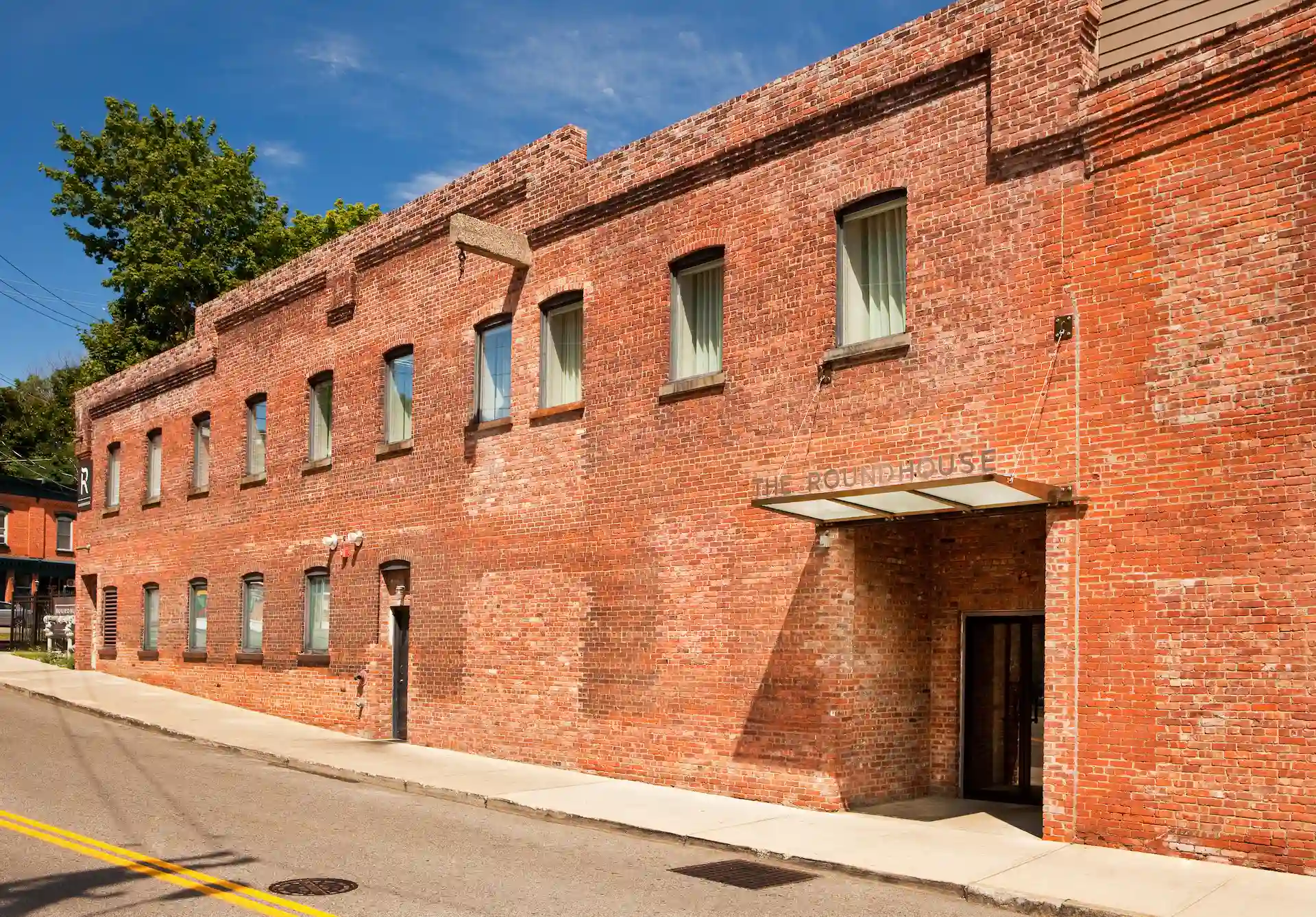 Brick exterior of the roundhouse building with street-level entrance and rows of windows under a clear blue sky.