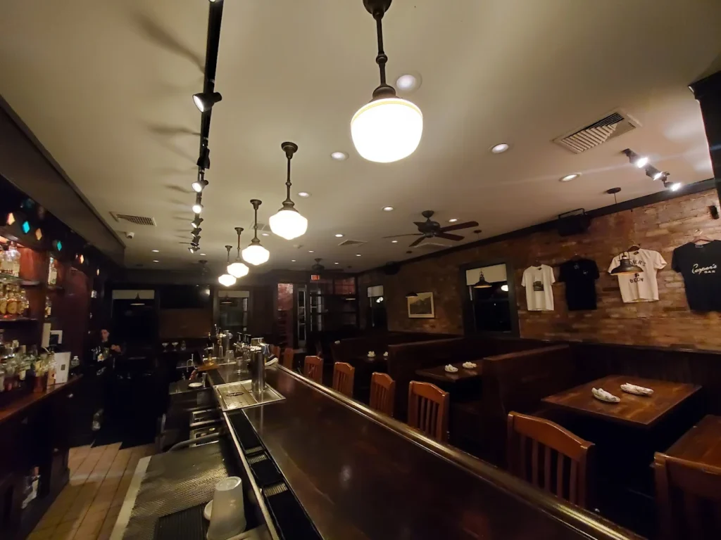 Cozy bar interior with wooden booths, brick walls, hanging lights, and a long bar counter.