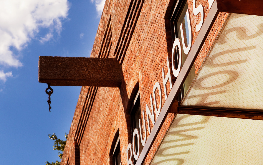 Close-up of a vintage “roundhouse” sign mounted on a red brick building against a blue sky.