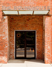 Brick entrance to the roundhouse with glass doors and metal canopy above, framed by red brick walls.