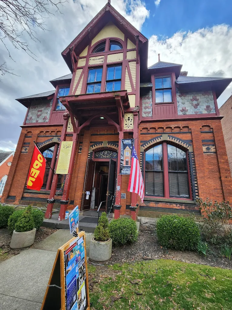 Historic brick museum building with red trim, gabled roof, flags, and open entrance.