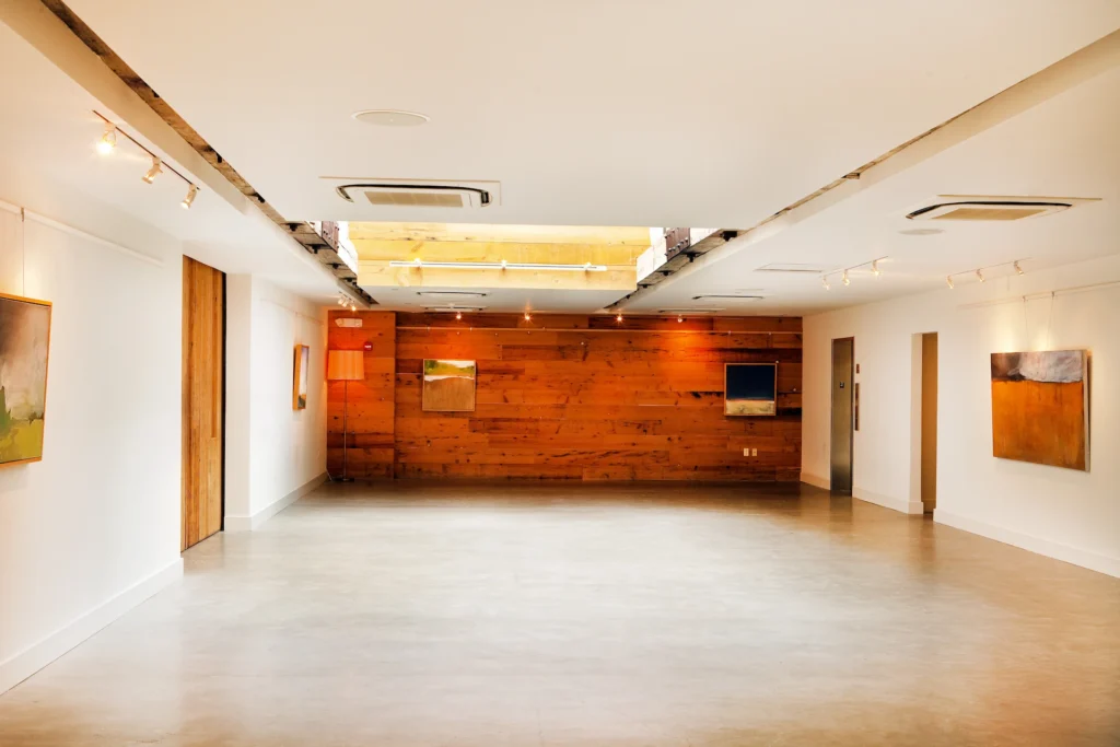 Spacious gallery-style room with polished floors, wood accent wall, skylight, and framed artwork on white walls.