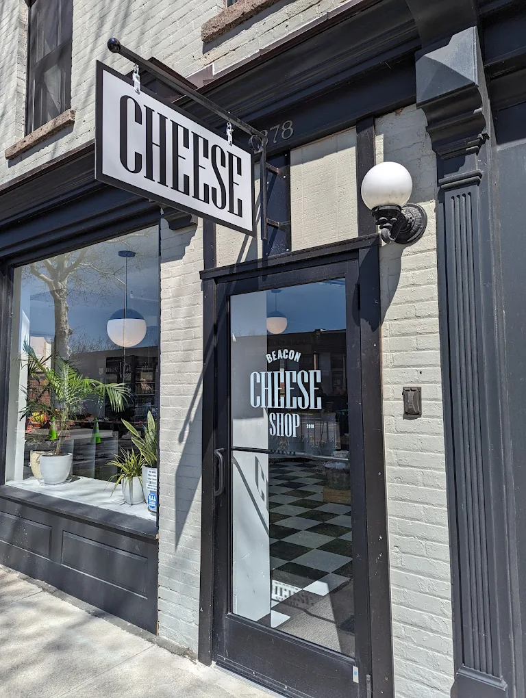 Beacon Cheese Shop storefront with hanging sign, glass door, and light brick exterior.