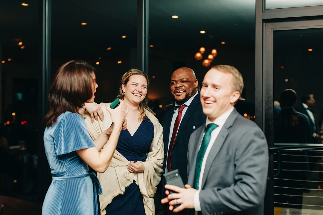 Wedding guests laughing and chatting together indoors during an evening reception.