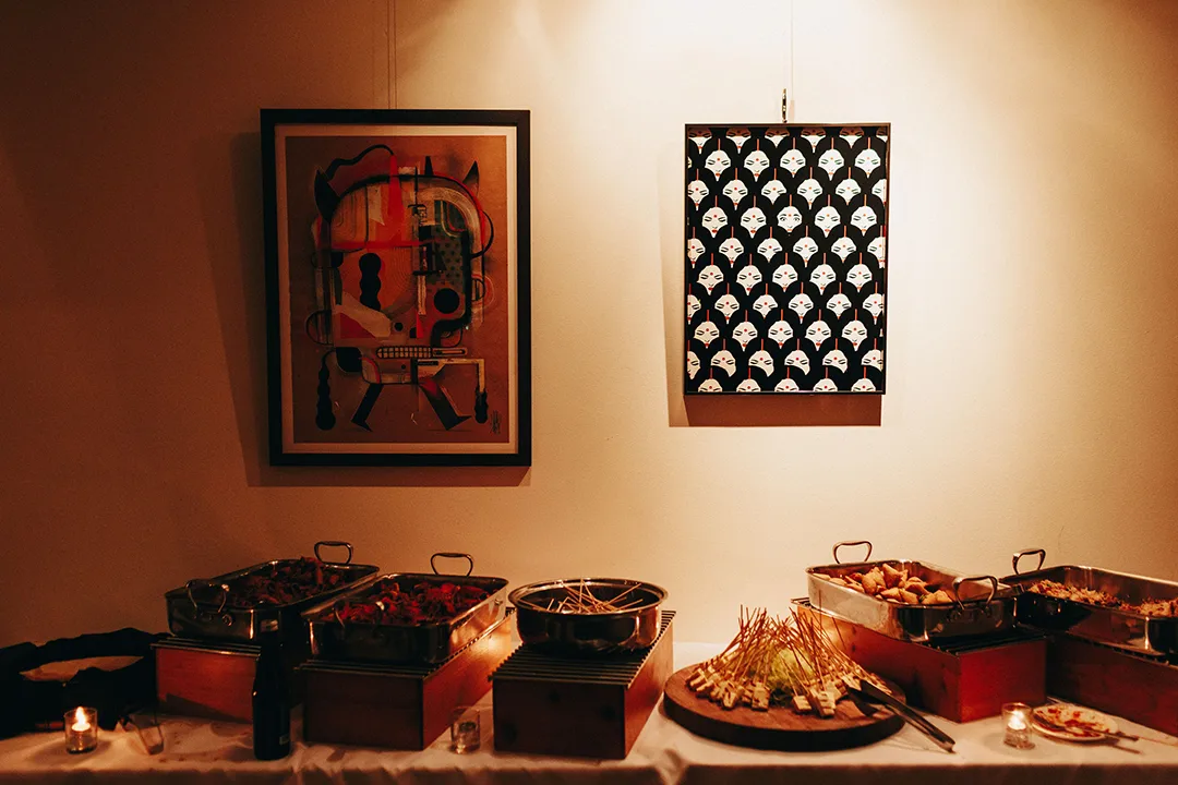 Buffet table with catered dishes beneath framed artwork in a warmly lit indoor space.