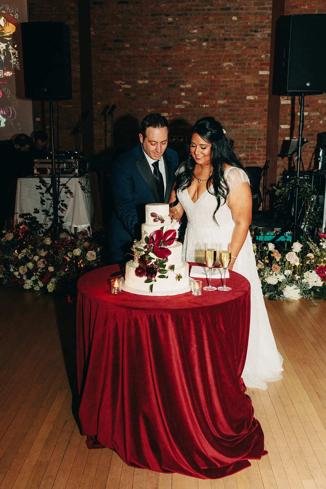 Bride and groom cutting a wedding cake at a reception table with champagne glasses.