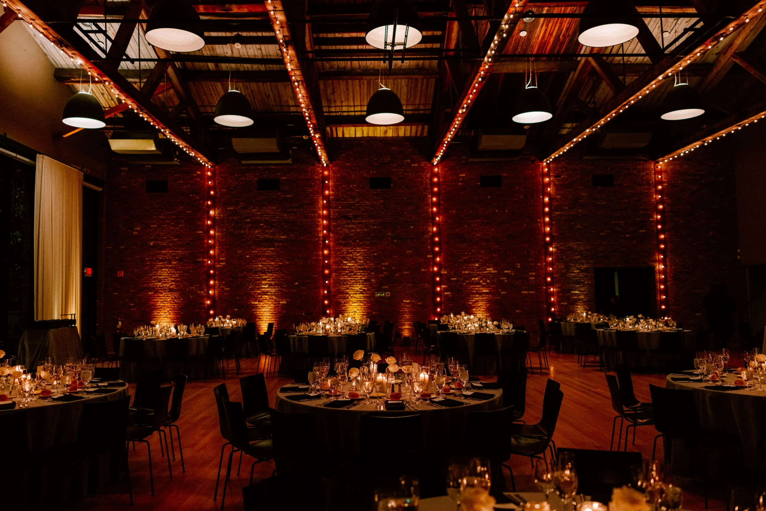 Elegant event hall with candlelit tables, exposed brick walls, and warm lighting.