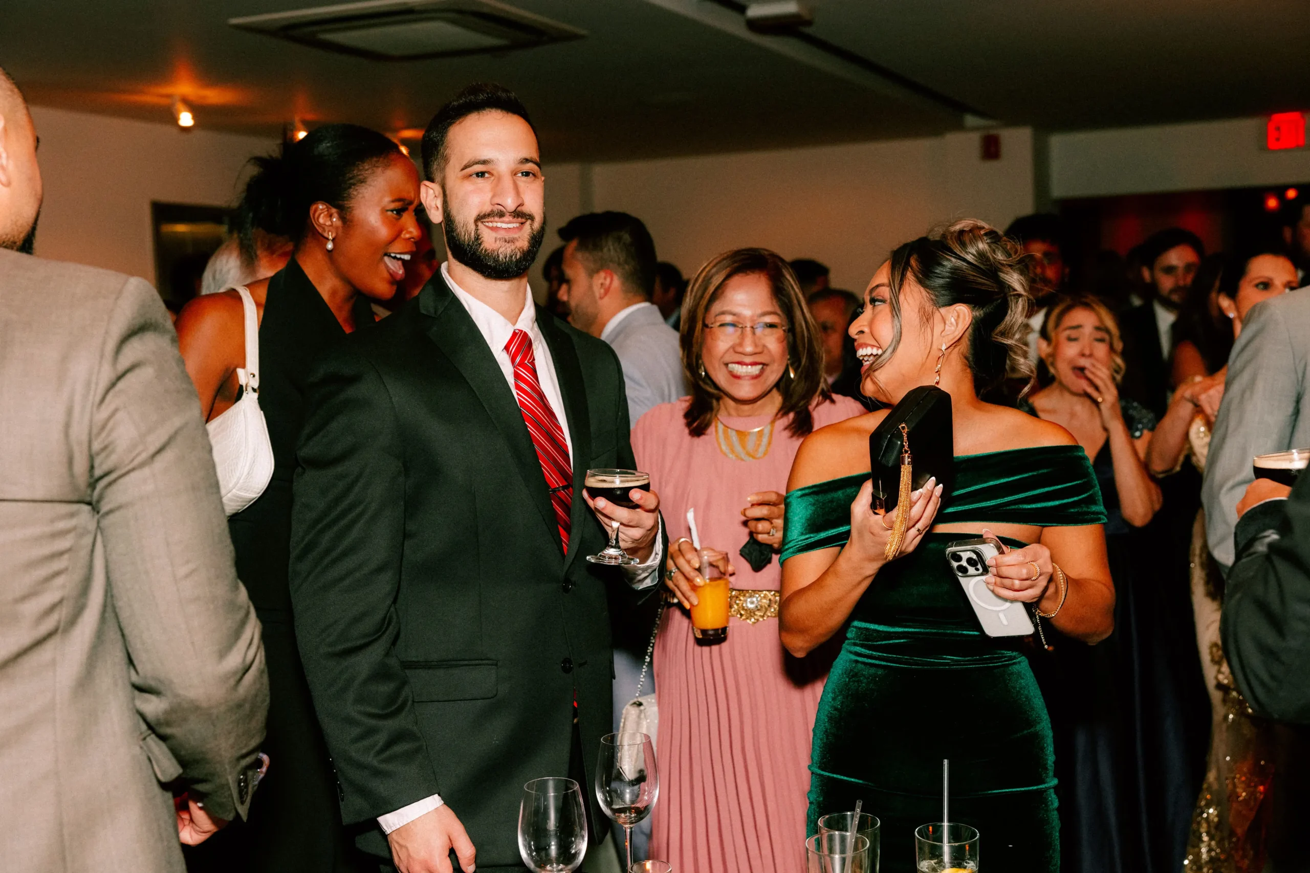 Guests laugh and toast at a lively wedding reception, dressed in elegant evening wear.