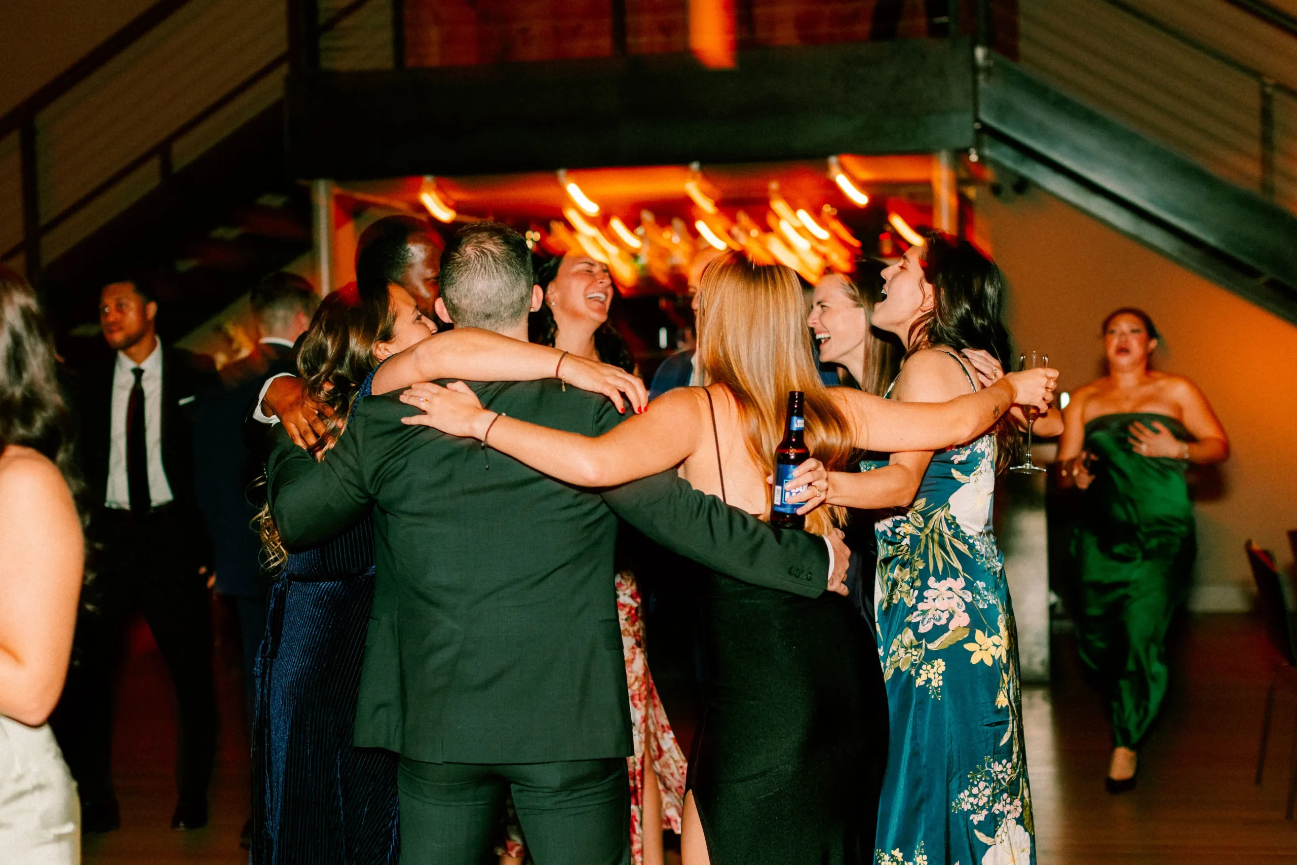 Guests hug and sing together on a lively dance floor during a wedding reception.