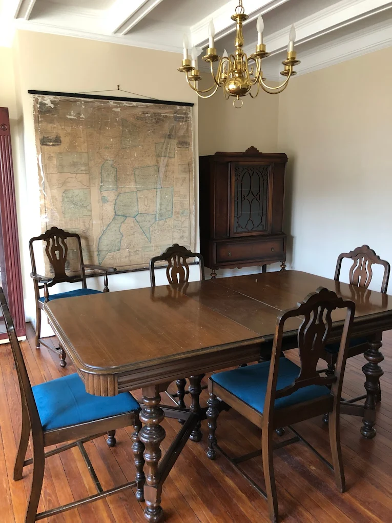 Historic dining room with wooden table and chairs, brass chandelier, and antique wall map.