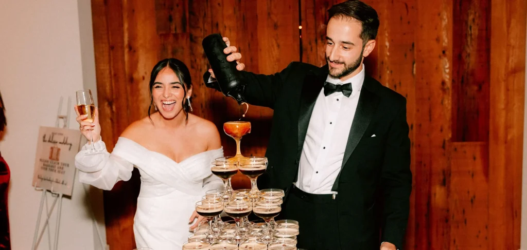 Bride and groom pour champagne into a stacked glass tower, celebrating at their wedding.