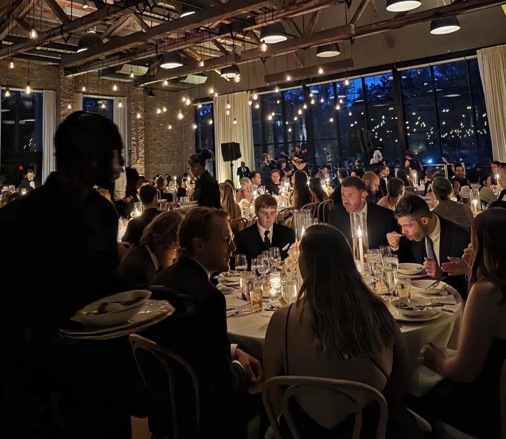 Guests seated at candlelit tables during a formal wedding reception in an industrial space with hanging lights.