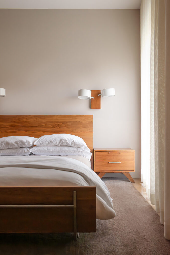 Minimalist bedroom with a wooden bed frame, white linens, matching nightstand, and soft natural light.