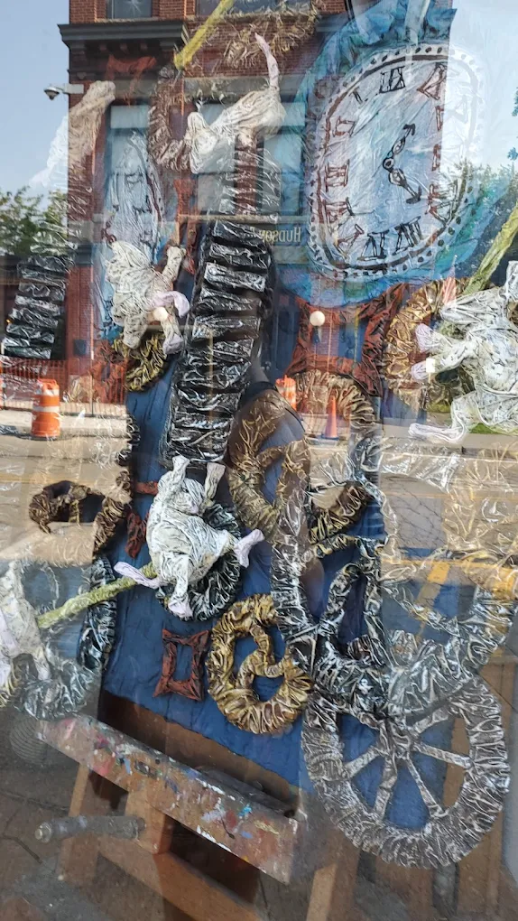 Abstract mixed-media artwork with clock face, gears, and figures seen through a storefront window.