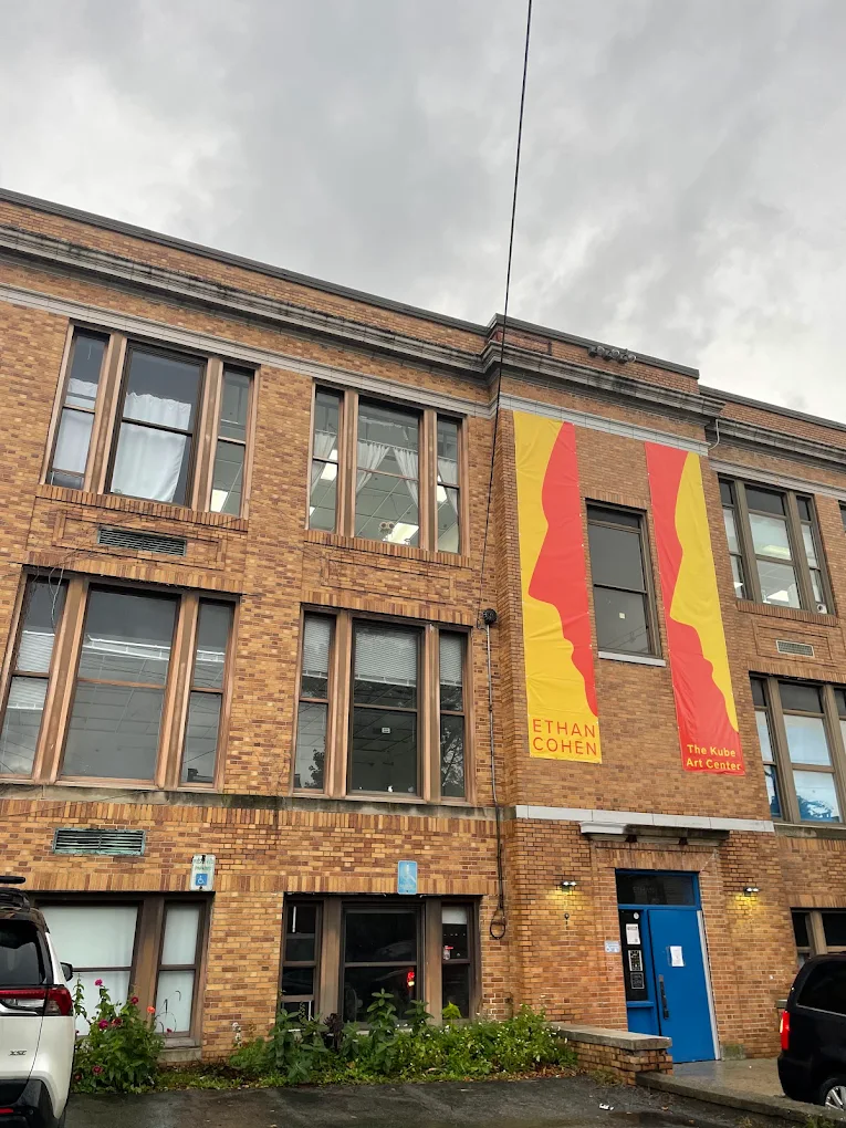 Brick art center building with yellow and red banners reading Ethan Cohen and The Kube Art Center.