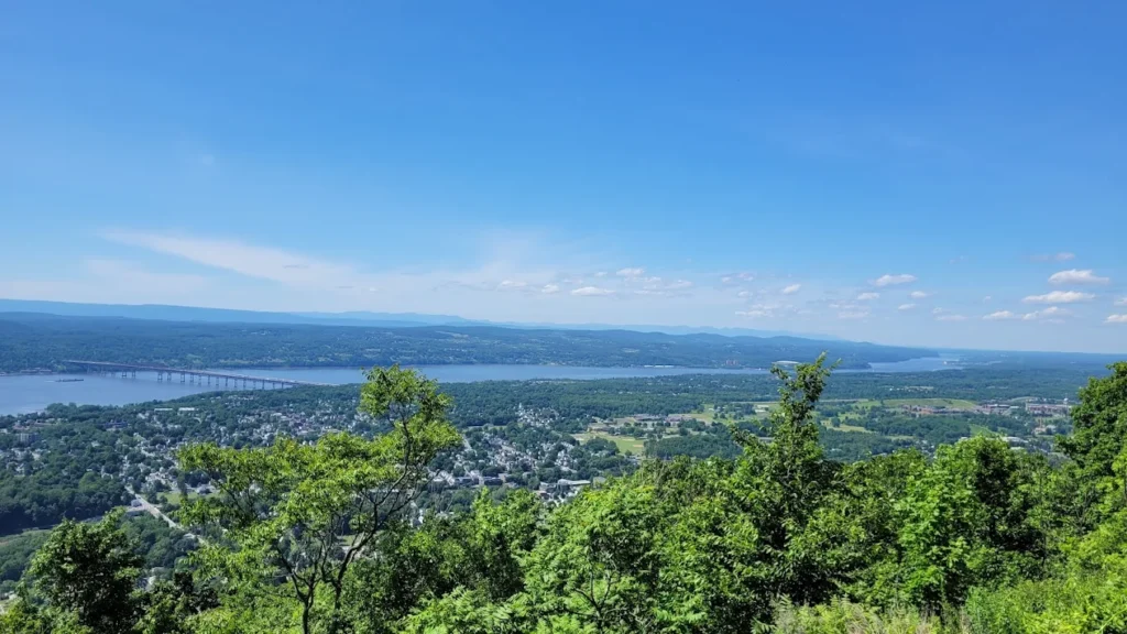 Panoramic hilltop view of a river, town, and rolling green landscape under a clear blue sky.