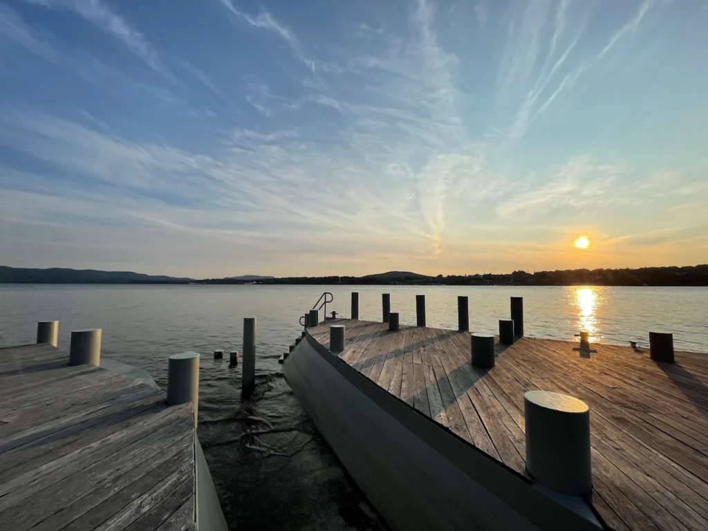 Curved wooden docks extending into calm water at sunset under a wide, streaked sky.