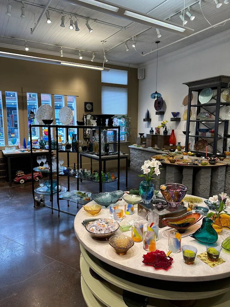 Glass art gallery interior with colorful bowls, vases, and sculptures on display tables.