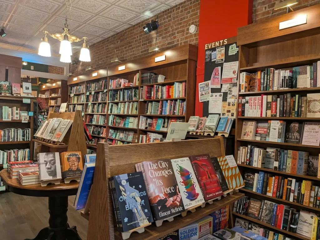 Independent bookstore interior with wooden shelves, featured books on display, and brick walls.