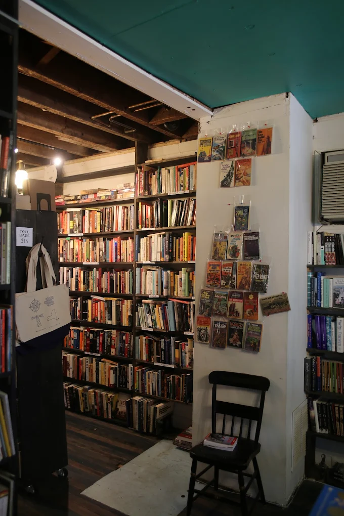 Cozy bookstore interior with tall shelves of books, hanging postcards, and a single black chair.