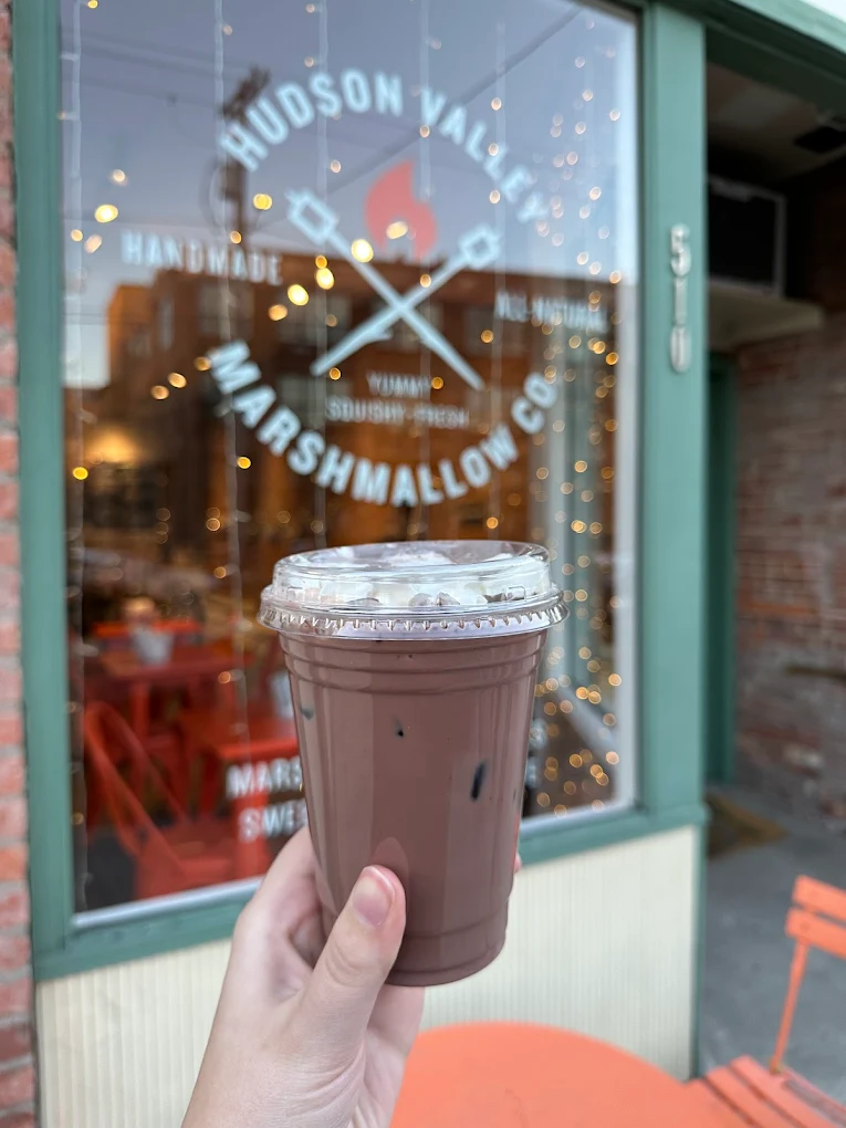 Iced chocolate drink held in front of Hudson Valley Marshmallow Co storefront window.