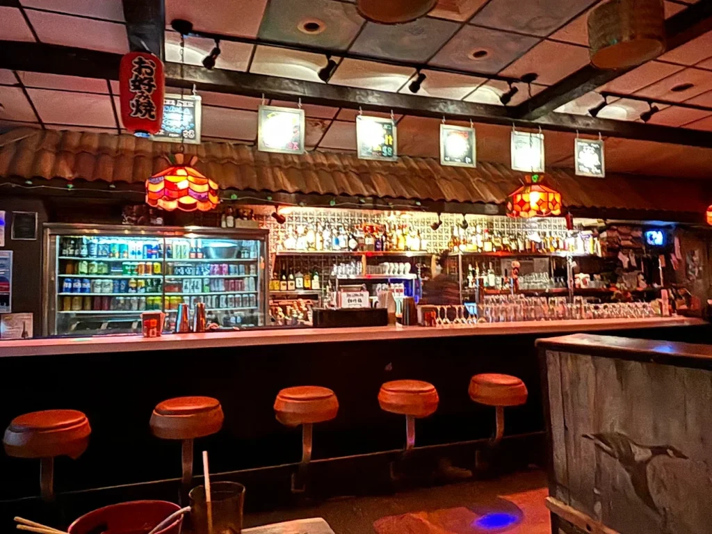 Retro-style bar with stools, neon lights, liquor shelves, and Japanese-inspired decor.
