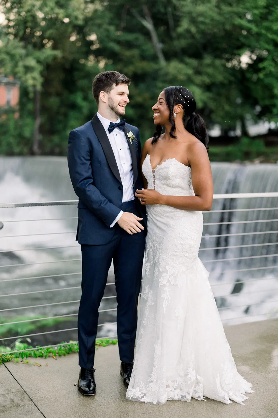 Bride and groom smiling together by a waterfall in formal wedding attire.