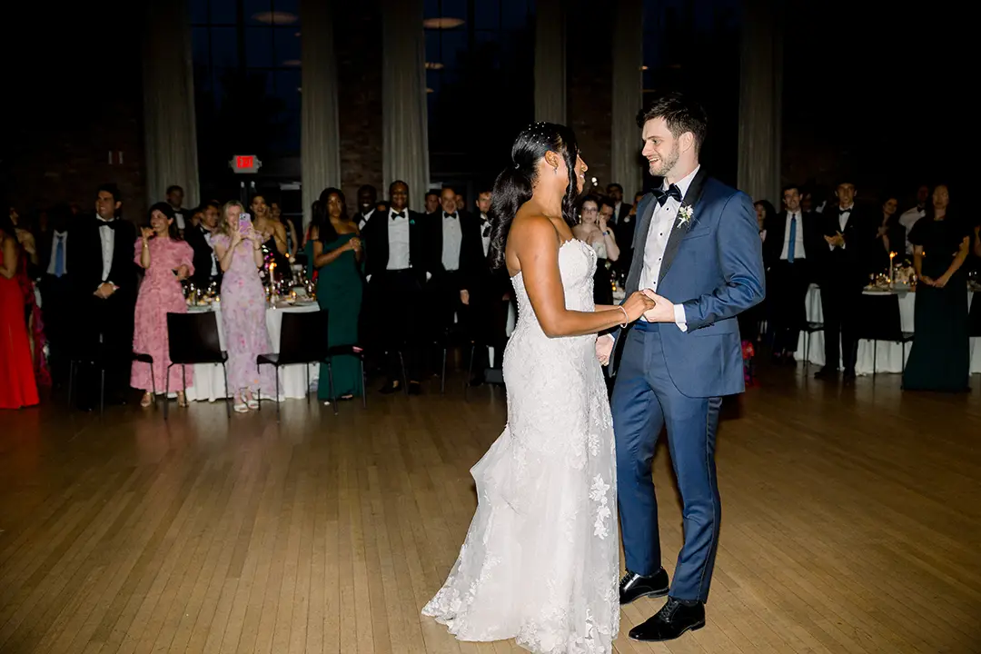 Bride and groom share first dance as guests watch in an elegant reception hall.