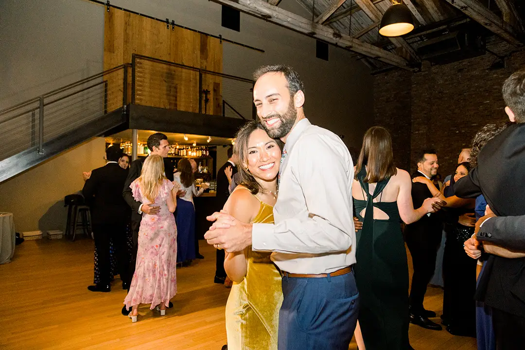 Guests dancing at a wedding reception in a rustic loft venue.