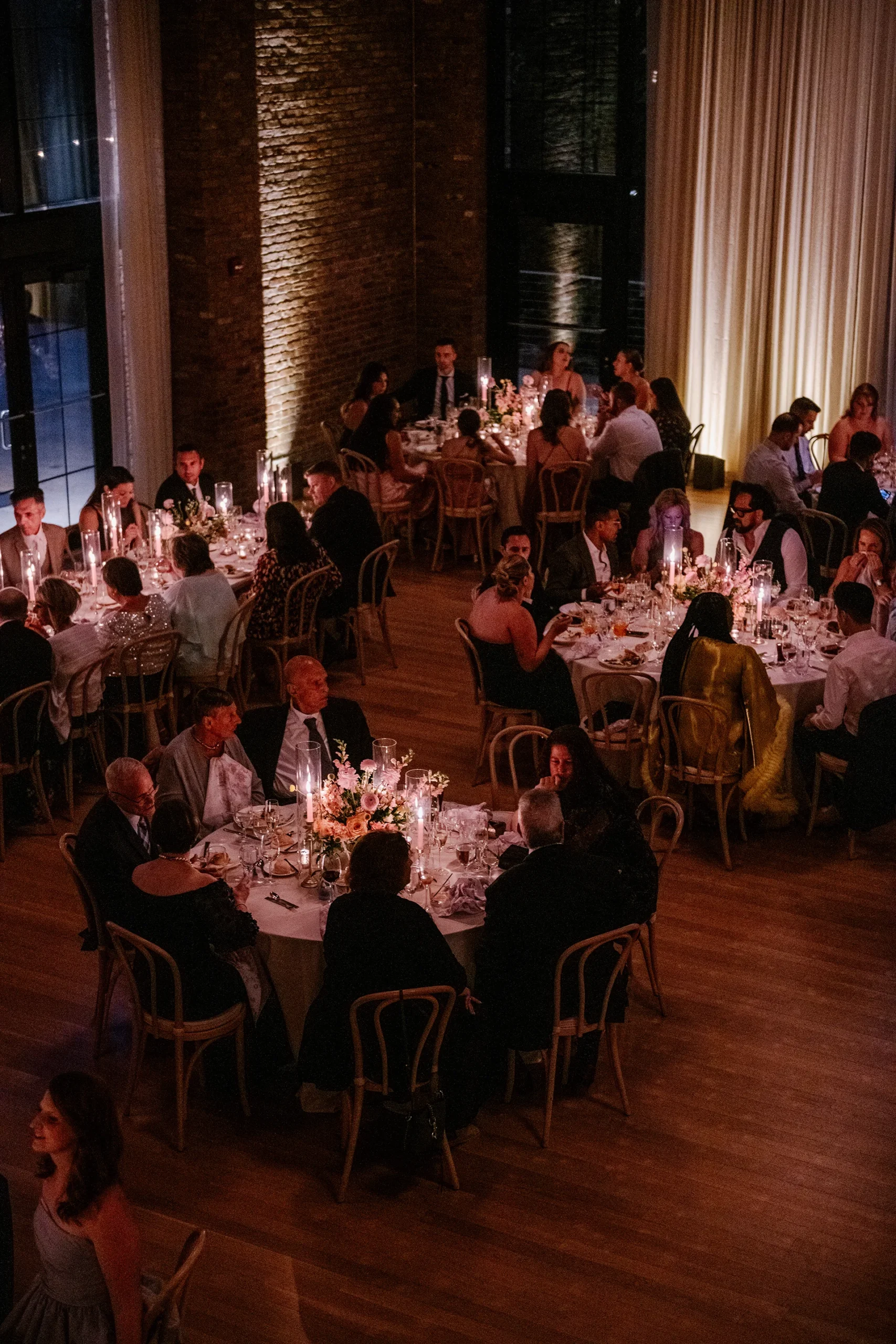Candlelit wedding reception with guests seated at round tables in a warmly lit indoor venue.