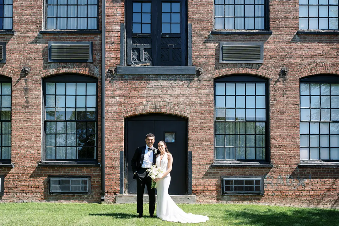 Wedding couple posing in front of a historic brick building on a sunny day.