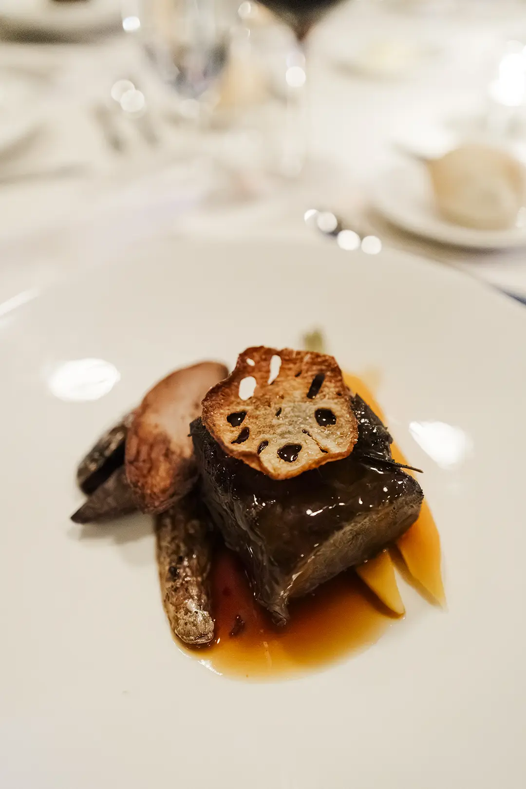 Plated gourmet dish with braised meat, roasted vegetables, and rich sauce on a white plate.