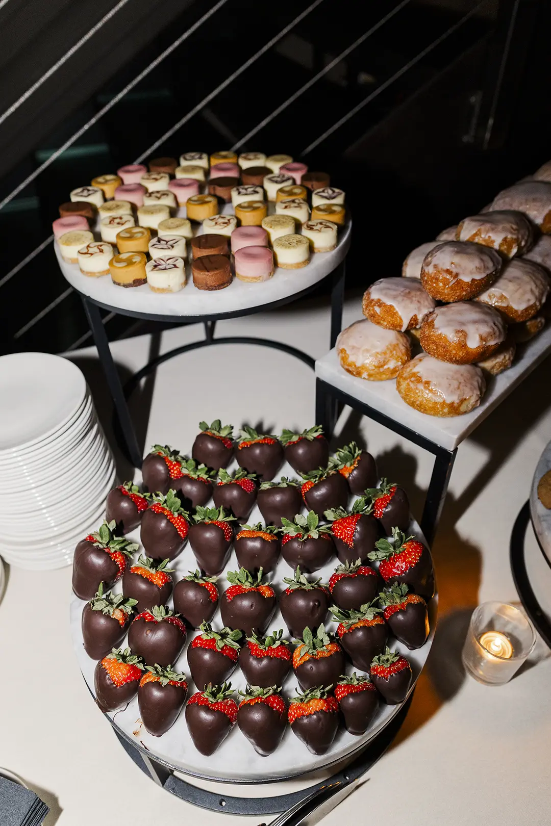 Dessert table with chocolate-covered strawberries, mini cheesecakes, and donuts.
